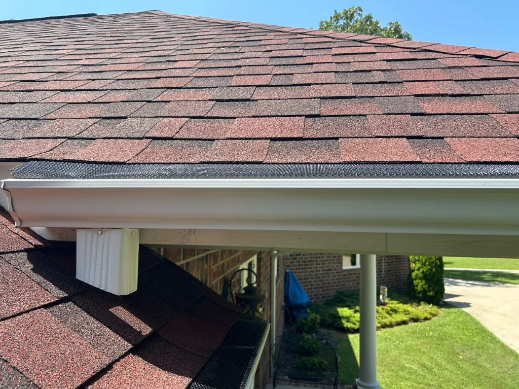 Clean residential gutter with mesh gutter guards along a shingle roof