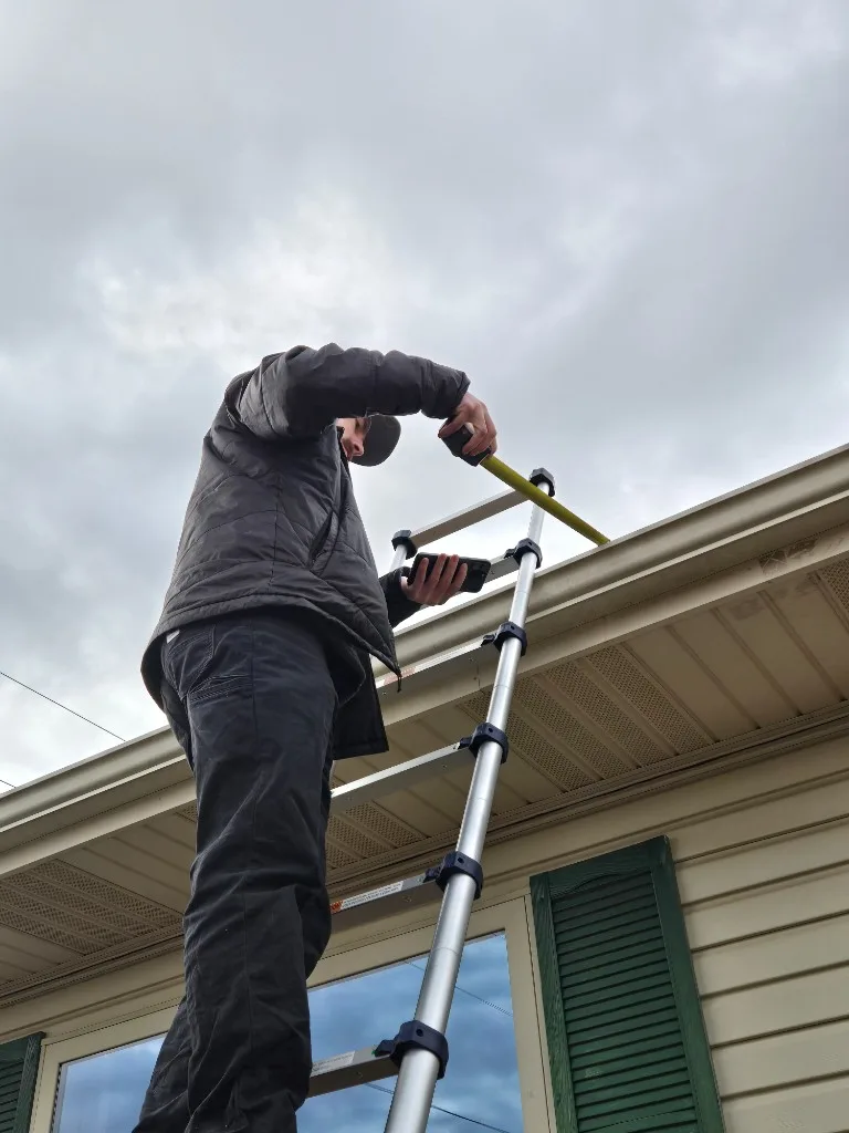 SRA technician on a ladder measuring a residential gutter